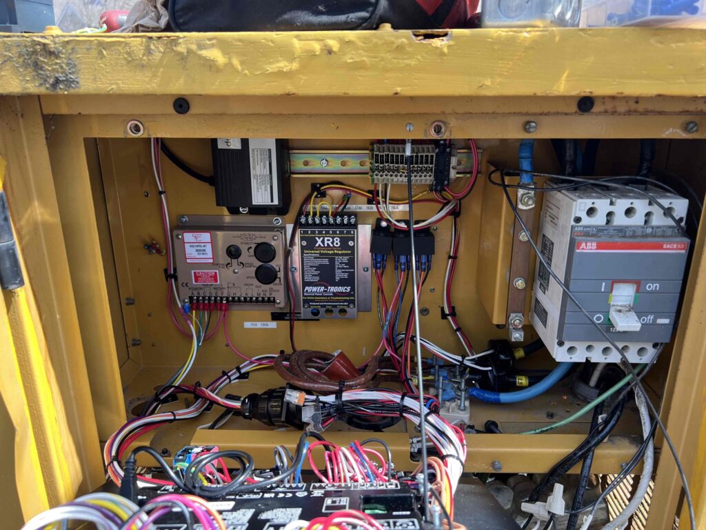 The control panel for a generator running while power on. Technician is inspecting wiring and sensors, checking for loose connections. 