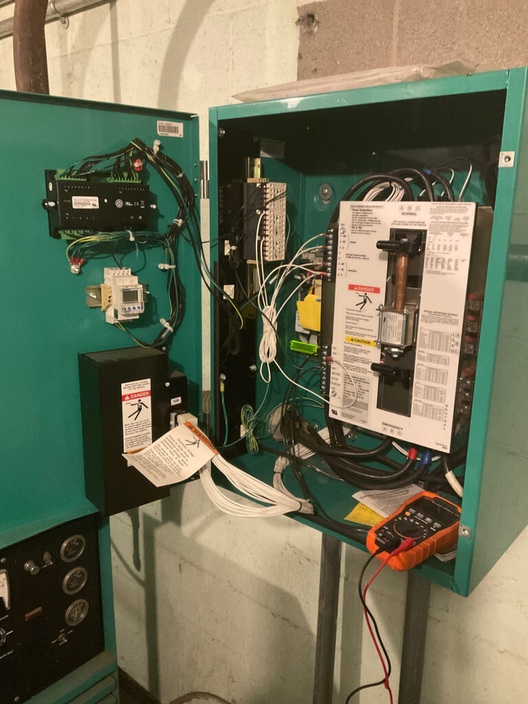 A close-up image of the internal workings of a Cummins transfer switch, showcasing its control panel, wiring connections, and switches. The transfer switch is installed at a university in New Jersey, ensuring proper power transfer during an outage."