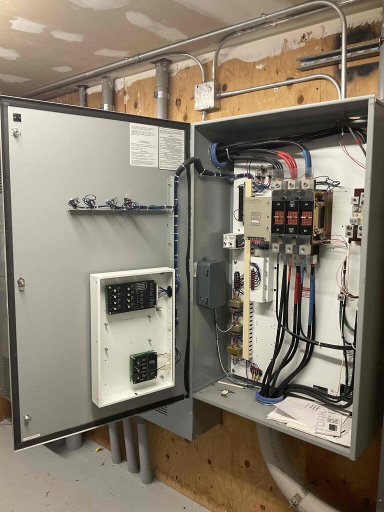 The internals of a transfer switch, showcasing its control panel, wiring connections, and switches. The transfer switch is installed in a hotel in Boston, Massachusetts, ensuring proper power transfer during an outage."