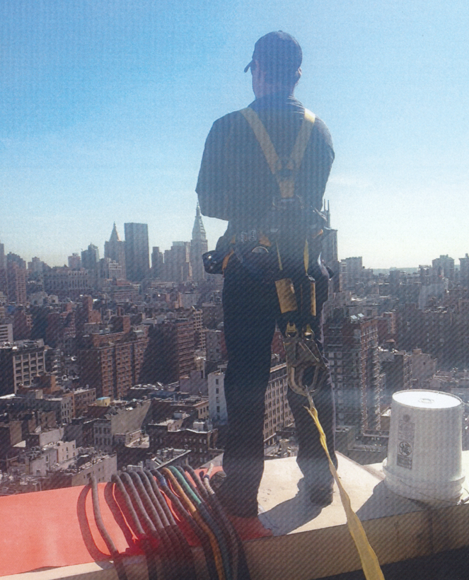 Weld Power Generator technician standing on the roof of a building in New York City. Power cables are hanging over the edge of the roof to the generator below.